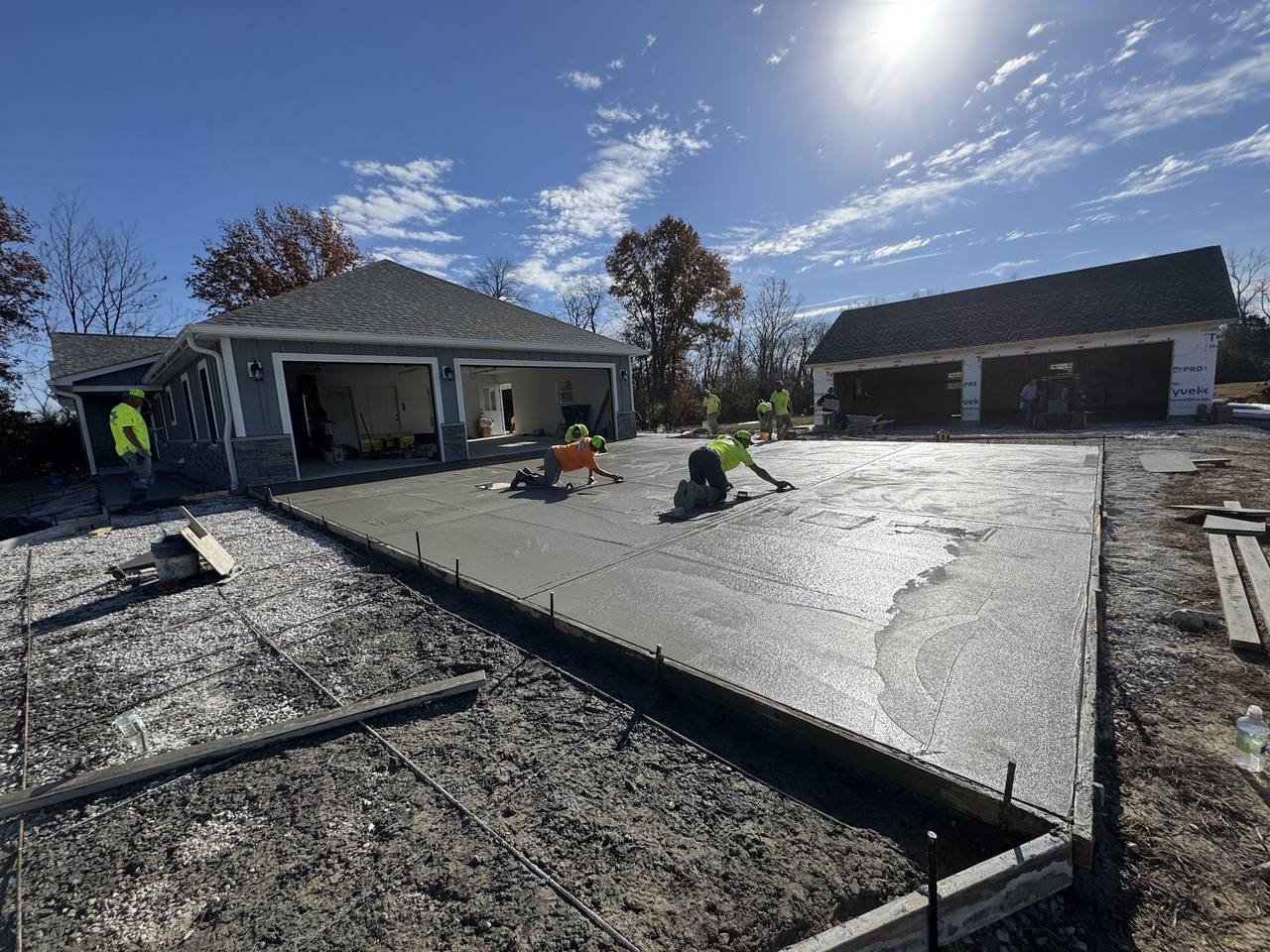 Crew hand finishing a wide fresh driveway pour at a newly built house